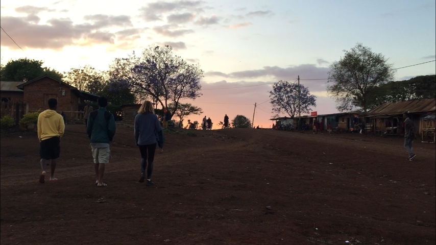      People walking on a rural dirt path during sunset.
  
