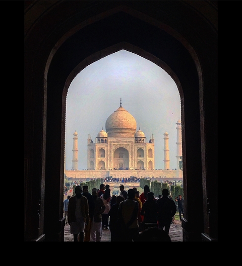 Daylight view of the Taj Mahal framed by an archway with visitors in the foreground.