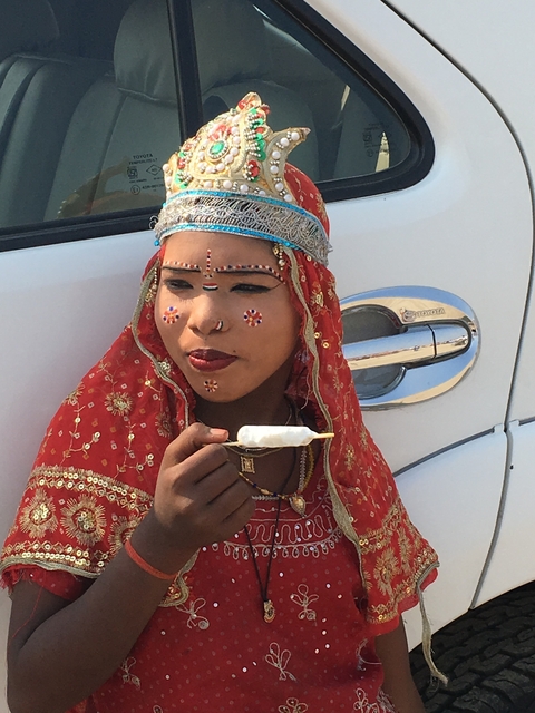       A woman in traditional attire enjoying an ice cream, sitting near a car.
  