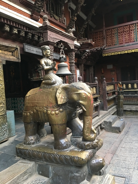 A brass statue of an elephant with a bell on top in a historic setting.