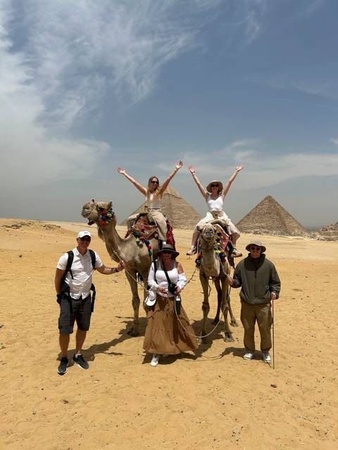 Group of people on a camel with pyramids in the background.