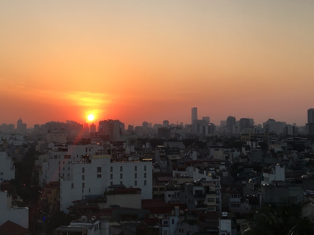       City skyline at sunset with the sun setting between buildings.
  