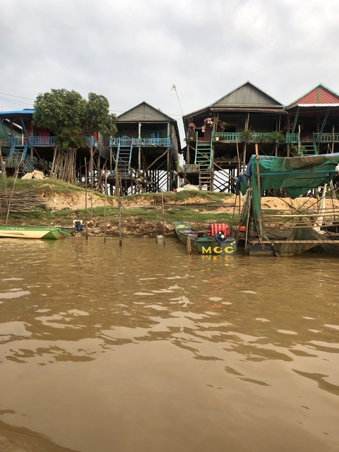       Stilt houses by a muddy riverbank with boats.
  