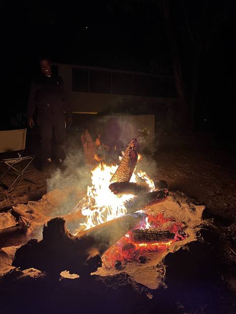       A campfire burning brightly with people nearby at night.
  