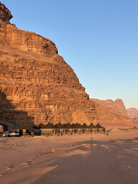Cliffside with tents below set in desert landscape.