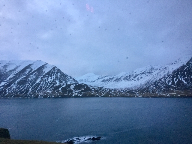 Snowy mountains with a large body of water beneath under a cloudy sky.