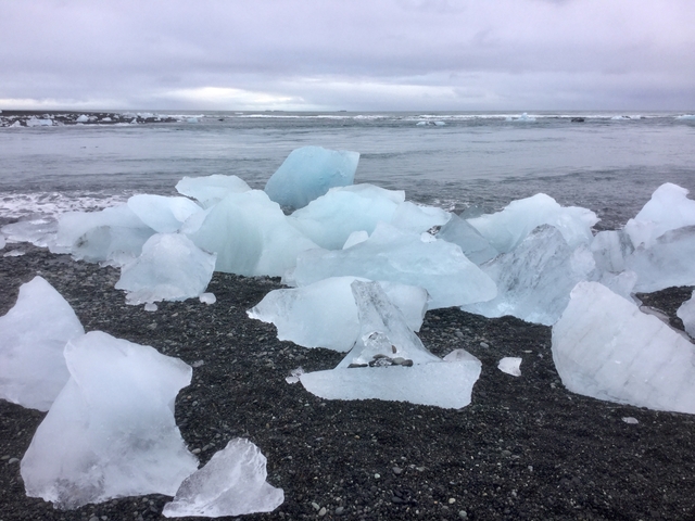 Ice chunks on a black sand beach with ocean waves in the background.