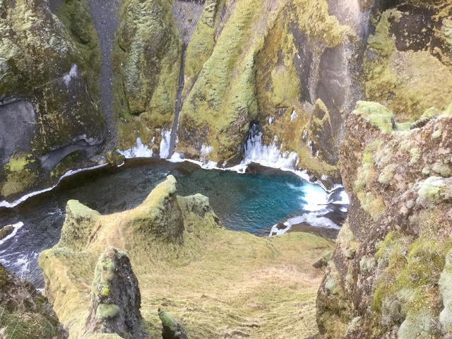 A turquoise pool of water surrounded by green and moss-covered rocks.