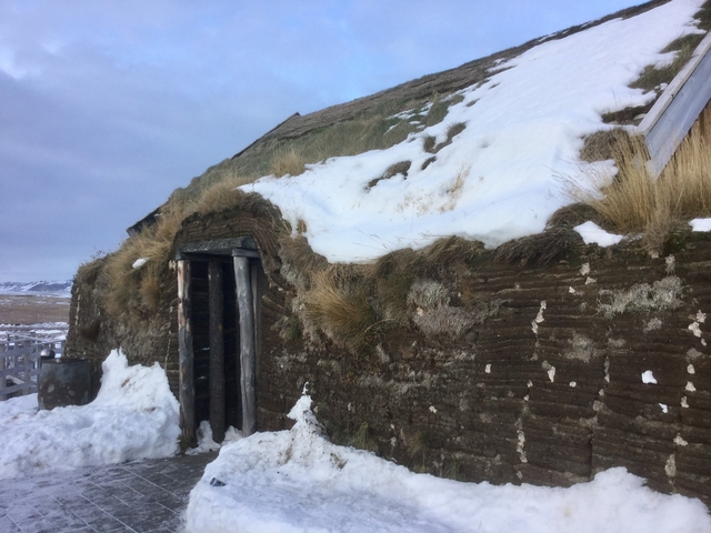 An old turf house partially covered in snow.