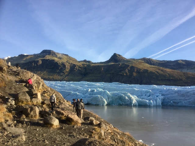 People hiking near a glacier with mountains in the background.