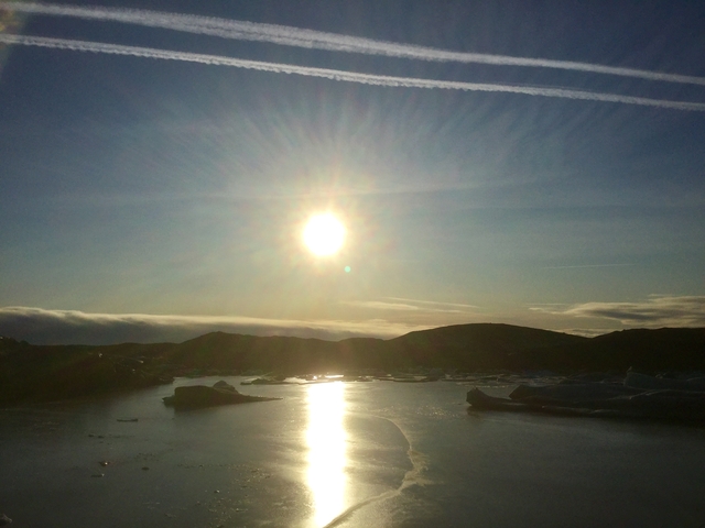 Sun shining over a water body with icebergs.