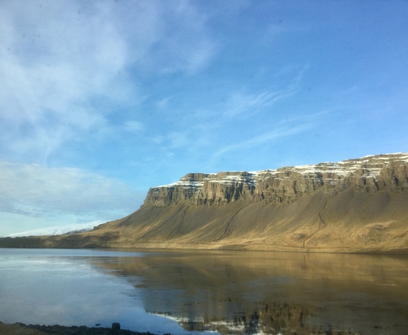 Majestic cliffs against a clear sky with water reflections.