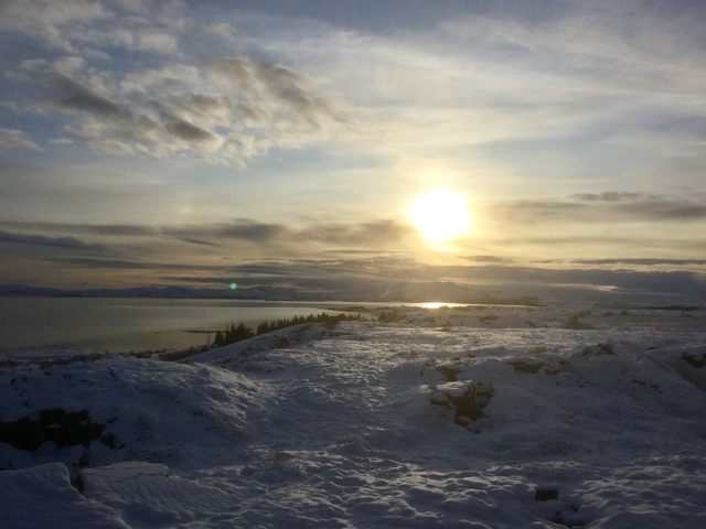 A snowy landscape with the sun setting over a body of water.