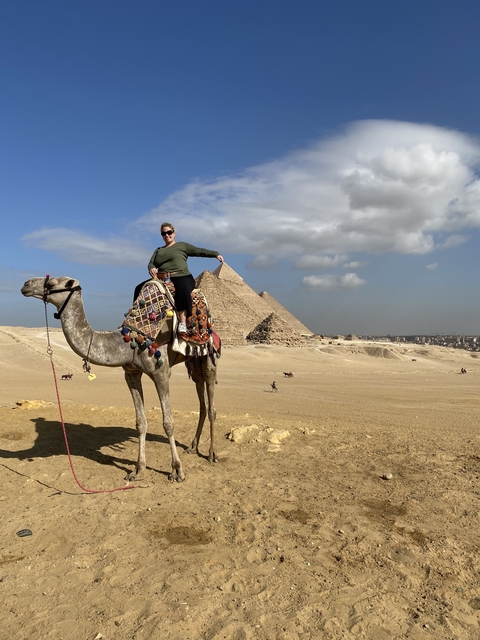      Person on camel with pyramids in the background.
  