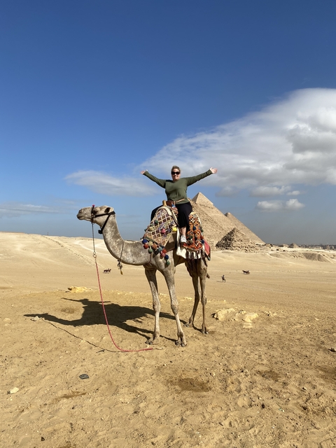       Person riding a camel in front of pyramids.
  