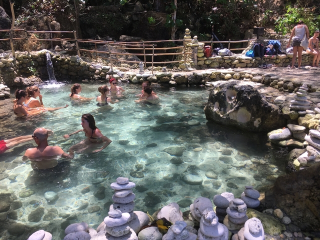       People enjoying a natural hot spring with a rocky surround.
  