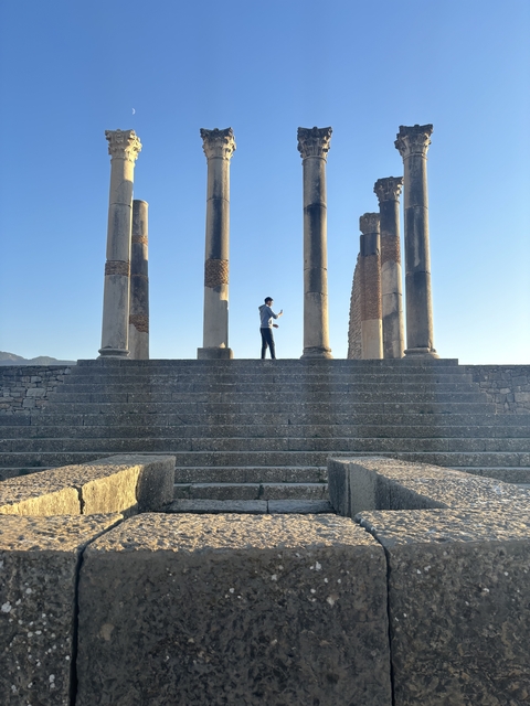 Person standing on ancient stone steps with columns in the background.