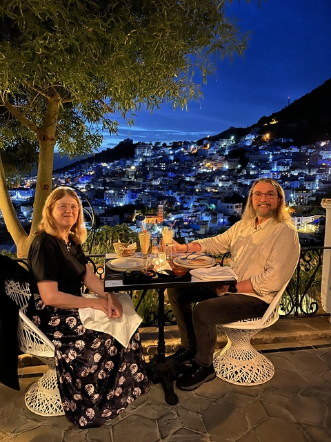 Couple dining outdoors with a view over a lit hillside city at night.