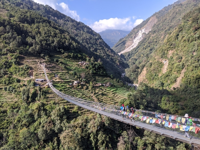 Suspension bridge with people, surrounded by terraced hills.