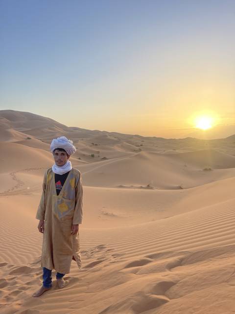       A person posing in traditional attire on desert dunes at sunset.
  