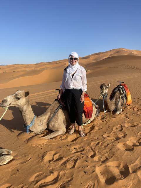       A person with a camel in a desert landscape.
  