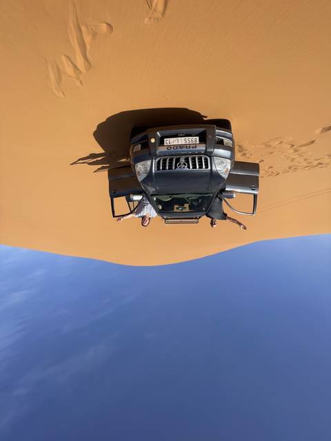       Car driving on sand dunes with people enjoying the scenery.
  