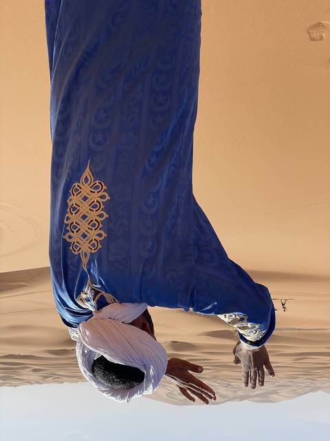       Person with traditional attire on sand dunes.
  