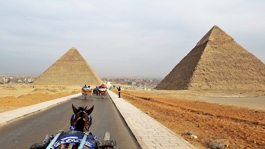 View of two pyramids and horse-drawn carriages on a road.