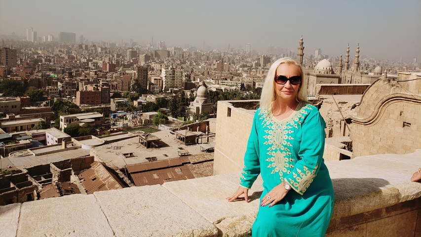 Person posing on a wall with a view of city and mosque in the background.