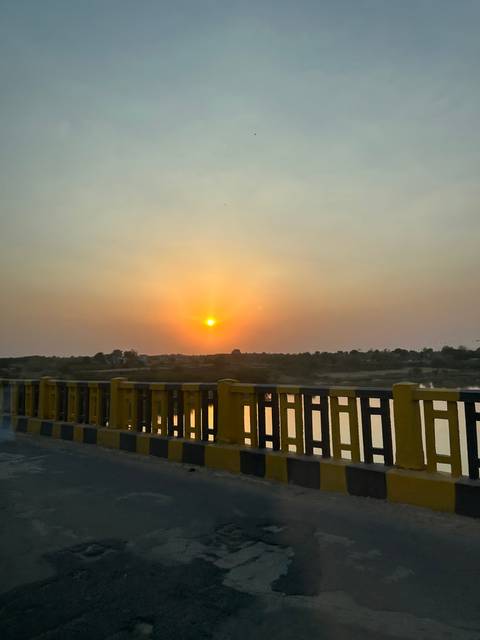       Sunset over a river with a railing in the foreground.
  