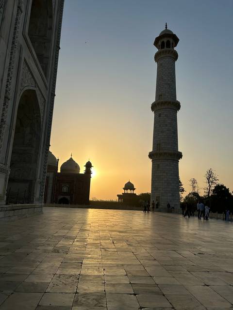       View of a minaret silhouetted against the sunset with people around.
  
