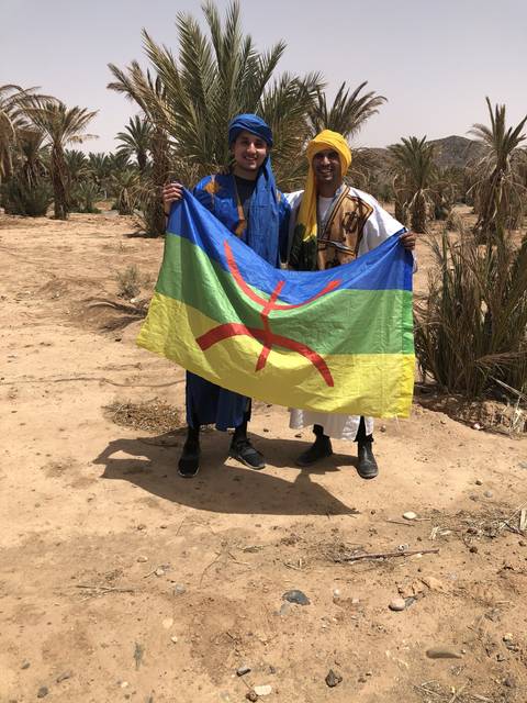       Two people displaying a colorful flag in the desert.
  