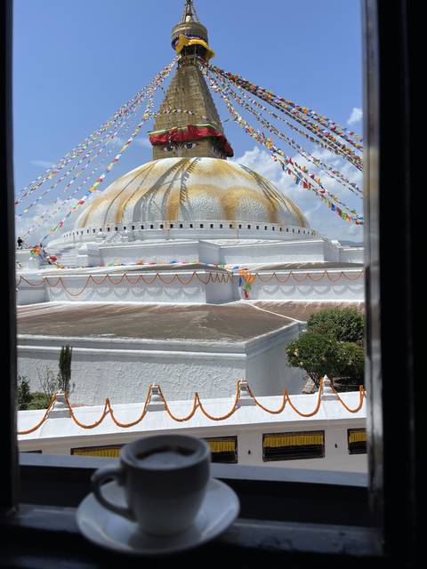 A stupa with colorful flags and a cup of coffee in the foreground.