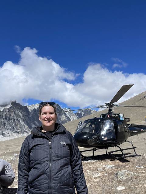 A person standing next to a helicopter with mountains in the background.