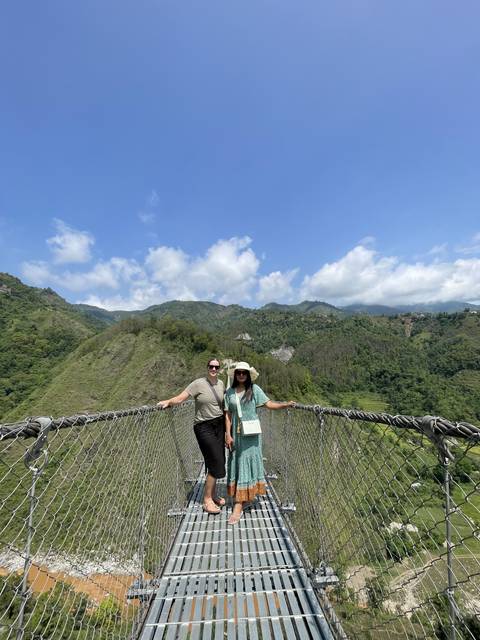 Two people standing on a suspension bridge with a scenic view.