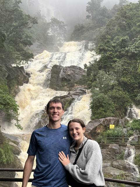       A couple posing in front of a waterfall.
  