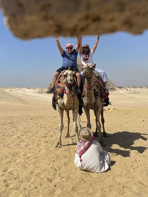       Two people on camels, one raising an arm.
  