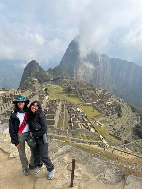 Two people smiling at Machu Picchu with a view of the ruins.