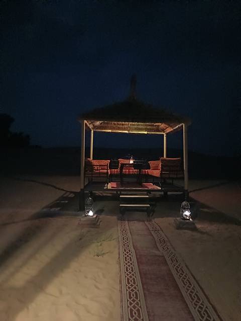       A nighttime setup with chairs and lanterns on sand.
  