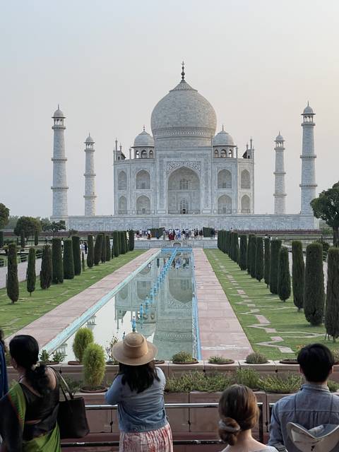       View of the Taj Mahal with tourists sitting nearby.
  