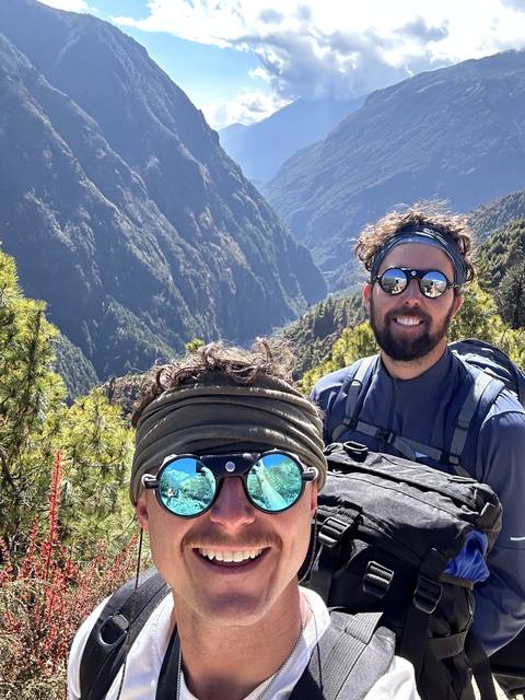 Two men with backpacks and sunglasses on a mountainous trail.