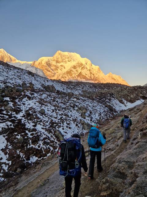       Hikers walking on a snowy trail with mountains.
  