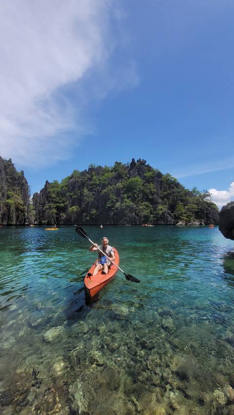       Person kayaking in clear blue waters surrounded by cliffs.
  