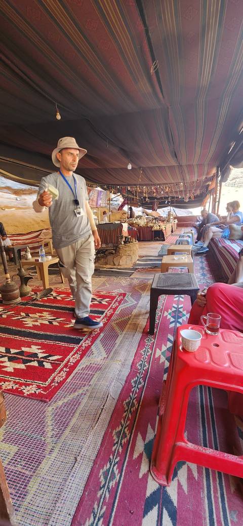Man inside a tent holding a drink with cultural decorations around.