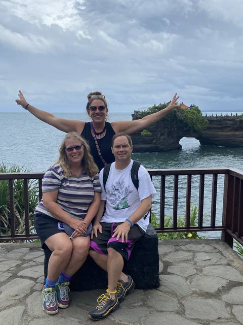 Three people posing by the sea with a temple in the background.