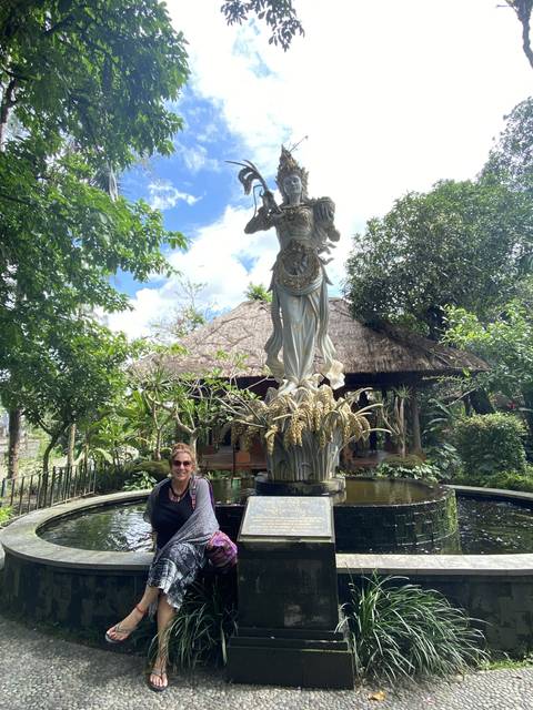 Person posing near a statue in a garden.
