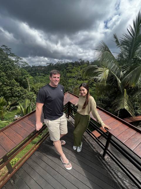 Two people on a wooden deck with tropical foliage.