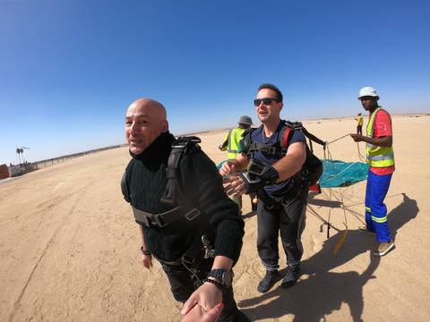       Couple of people preparing for skydiving on a sandy landscape.
  