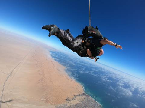       Skydivers in tandem above a desert and ocean landscape.
  