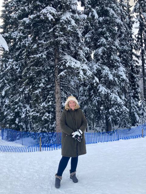       Person in a winter coat posing in front of snow-covered trees.
  